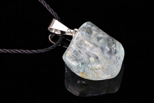 A silver-toned pendant with a clear, pale blue stone on a dark cord against a black background.