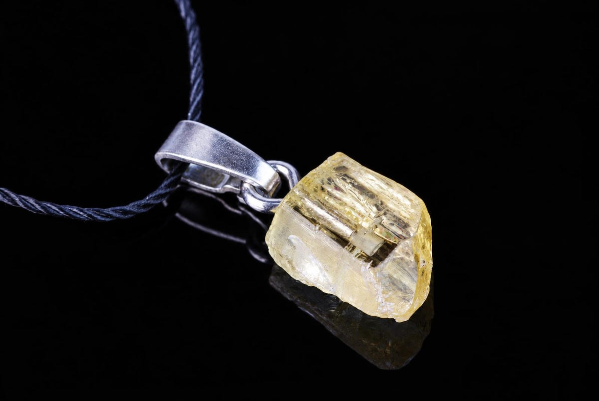 A yellow, faceted crystal pendant on a dark cord with a silver-toned bail, set against a black reflective surface.