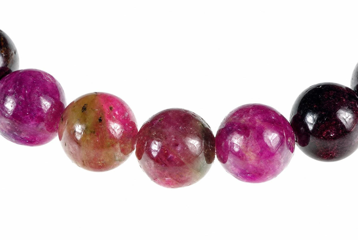 A row of round tourmaline beads in pink, purple, green and dark red on a white background.