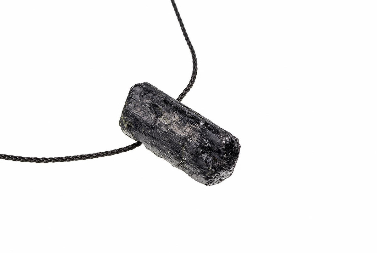 A black, raw tourmaline crystal pendant on a dark cord against a white background.