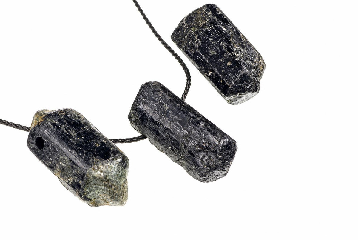Three raw black tourmaline crystals on a dark cord against a white background.