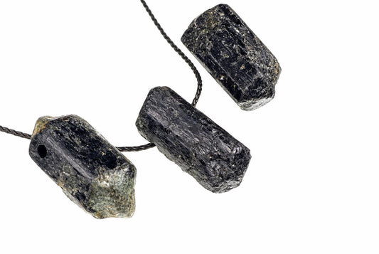 Three raw black tourmaline crystals on a dark cord against a white background.