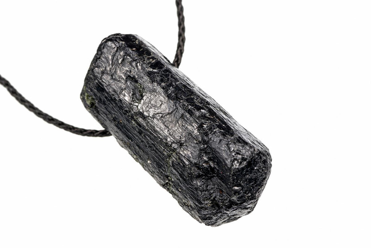 A raw black tourmaline crystal pendant on a dark cord, set against a white background.