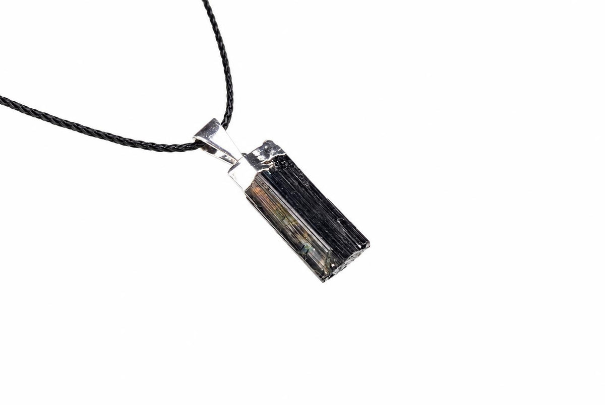 A rectangular tourmaline pendant with a silver-toned bail hangs from a black braided cord against a white background.