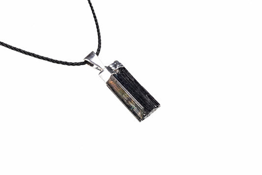 A rectangular tourmaline pendant with a silver-toned bail hangs from a black braided cord against a white background.