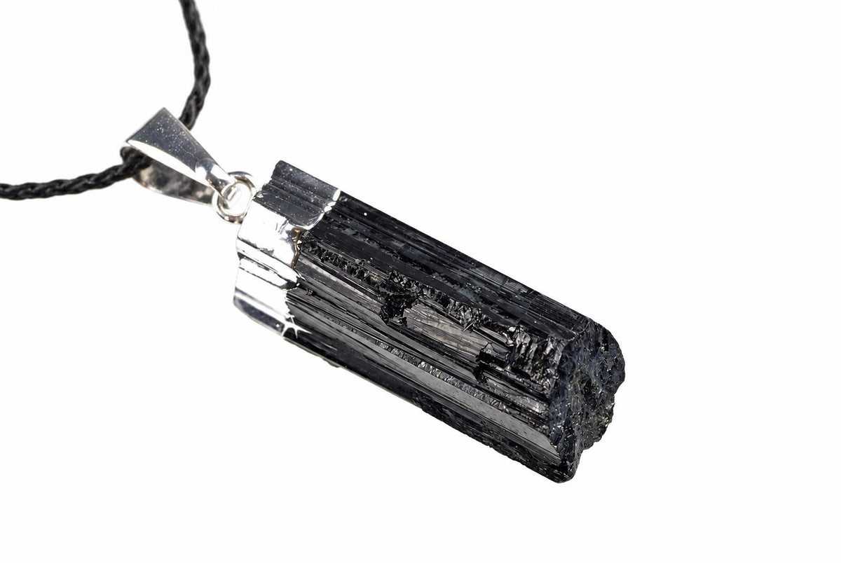 A silver-toned pendant with a dark, striated crystal on a black cord against a white background.