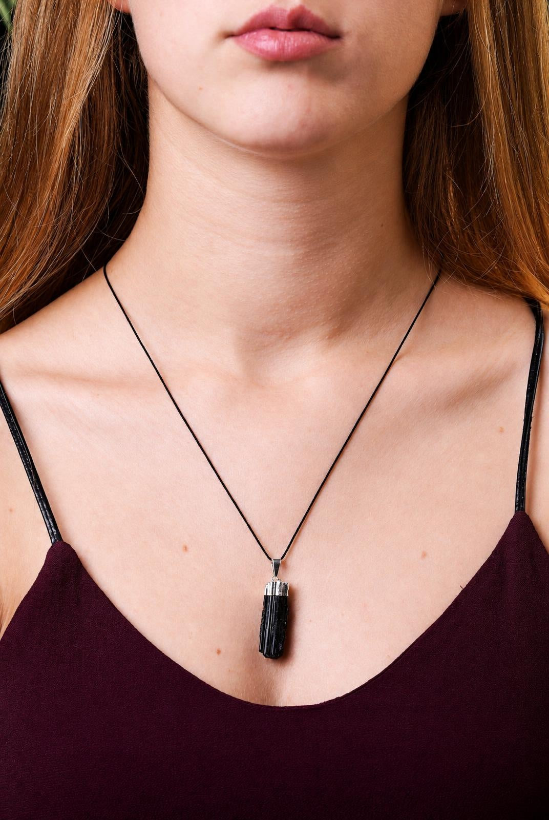 A person wears a necklace with a black, faceted pendant on a thin cord against a dark top.