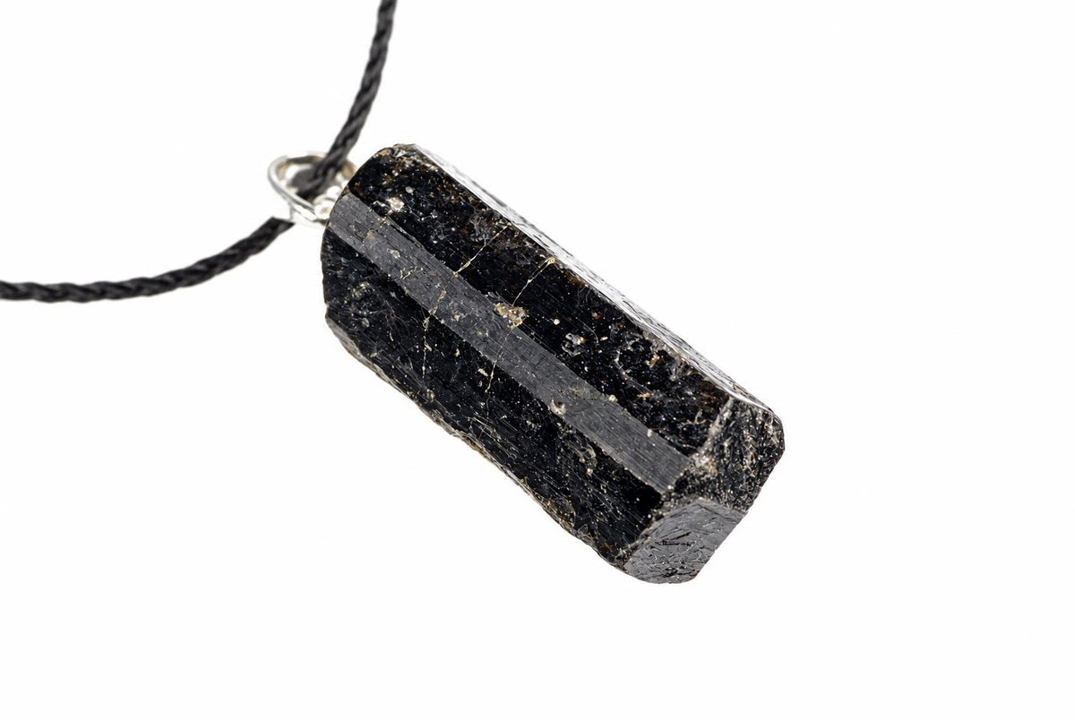 A black tourmaline crystal pendant on a dark cord, set in silver-toned metal against a white background.