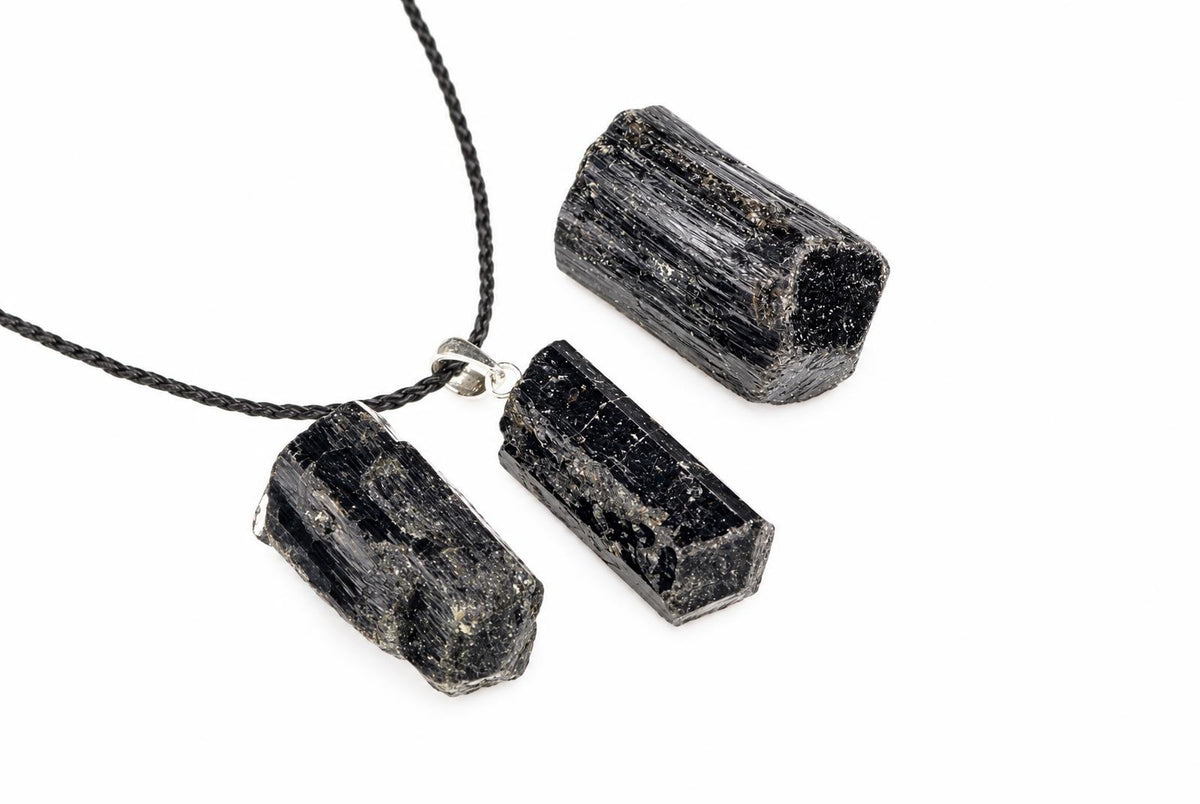 Rough black tourmaline pieces show ridged surfaces, with one silver mounted pendant attached to a black cord on a white background.