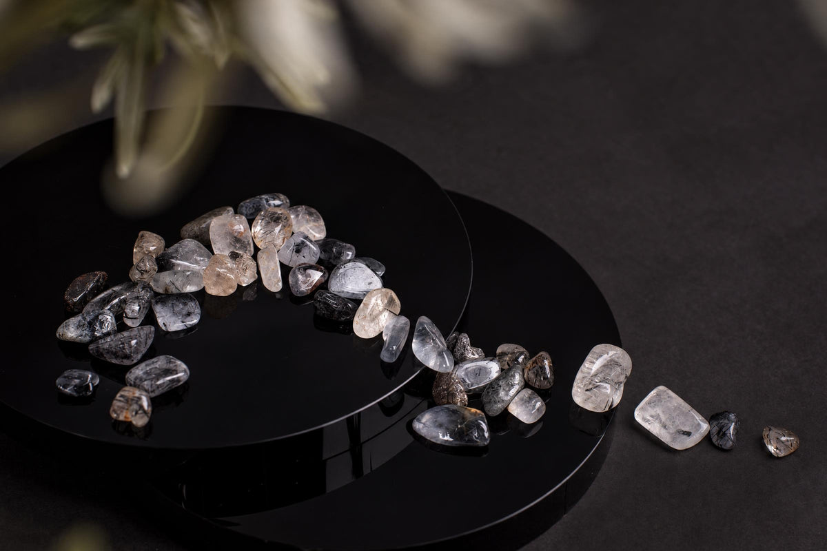 Polished tourmaline quartz stones in clear, grey and black tones arranged on a dark surface.