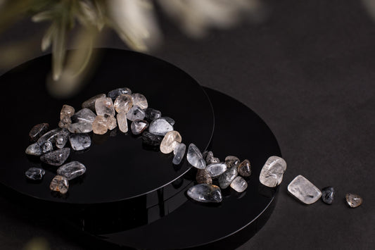 Polished tourmaline quartz stones in clear, grey and black tones arranged on a dark surface.