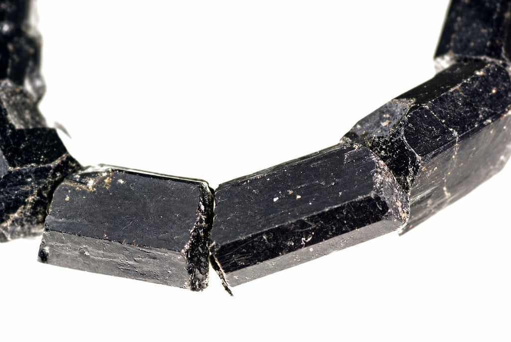A bracelet made of raw, dark black tourmaline schorl crystals with a rough, faceted surface on a white background.
