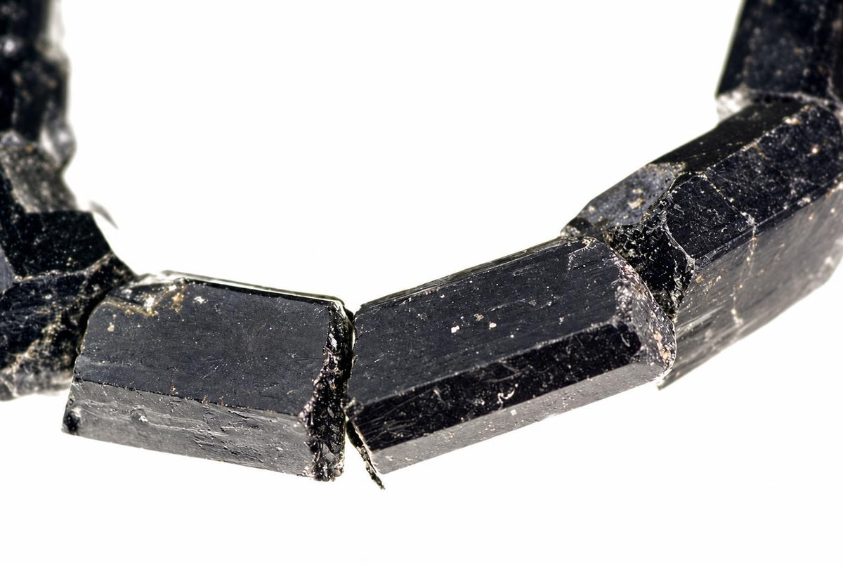 A bracelet made of raw, dark black tourmaline schorl crystals with a rough, faceted surface on a white background.