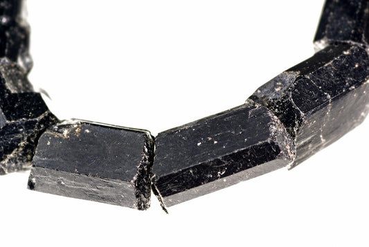 A bracelet made of raw, dark black tourmaline schorl crystals with a rough, faceted surface on a white background.
