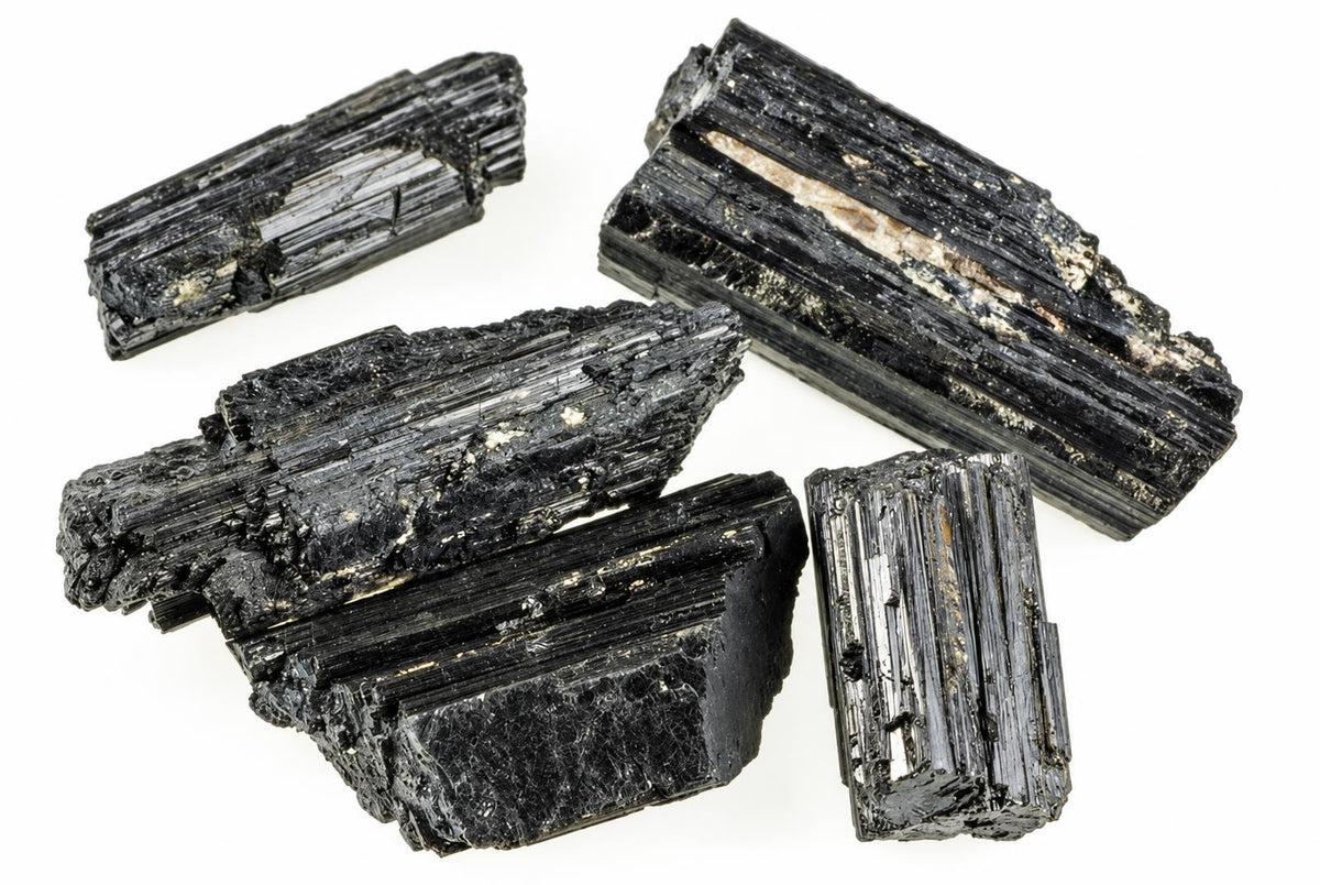 Four pieces of black Tourmaline schorl with visible striations and light inclusions on a white background.
