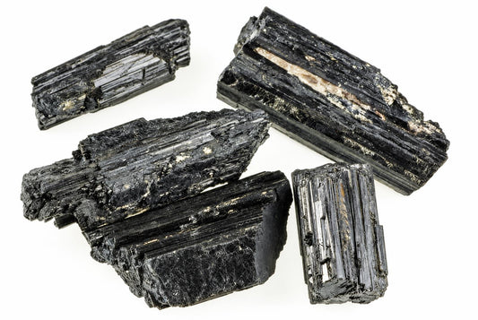Four pieces of black Tourmaline schorl with visible striations and light inclusions on a white background.