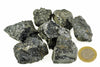 Several dark grey to black rough mineral pieces with a metallic sheen are arranged on a white surface next to a one euro coin.