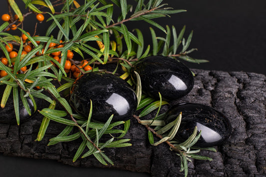 Three polished black stones rest on a dark wooden surface, surrounded by green leaves and small orange berries.