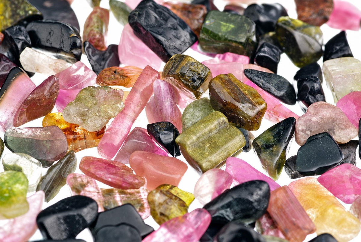 A collection of small, polished tourmaline stones in pink, green, black and brown on a white surface.