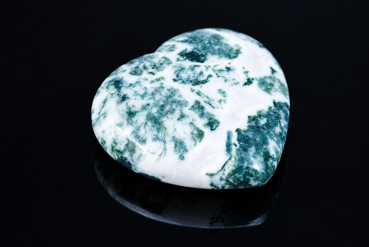 A polished heart-shaped stone with white and green mottled patterns rests on a dark, reflective surface.