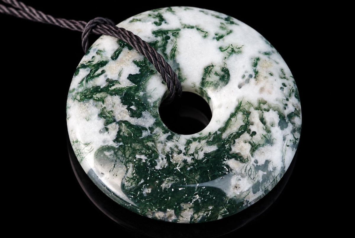 A polished, donut-shaped pendant with white and green marbled patterns on a dark surface, threaded with a brown cord.