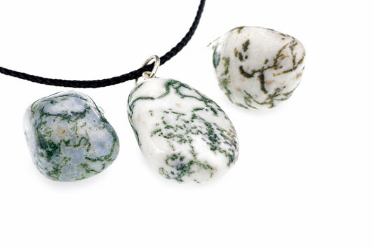 Three polished pebble pendants with green and white patterns on a black cord against a pale surface.