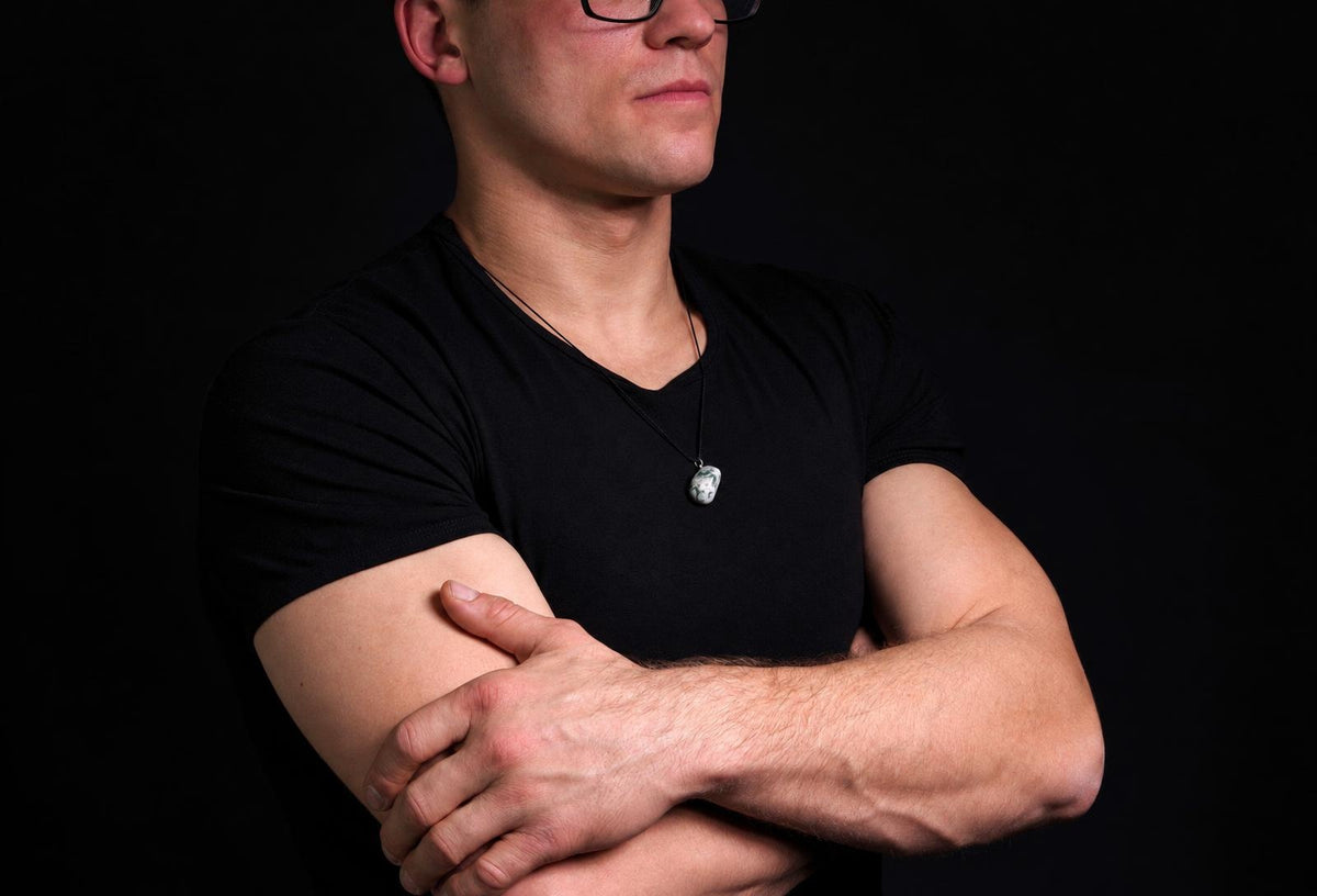 A man in a black t-shirt wears a pendant with a white and green patterned stone on a dark surface.