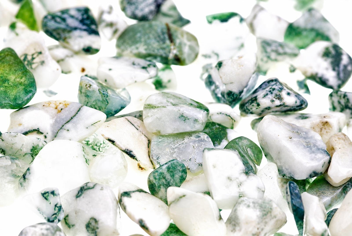 A pile of small, polished tree agate stones with white and green patterns on a bright surface.