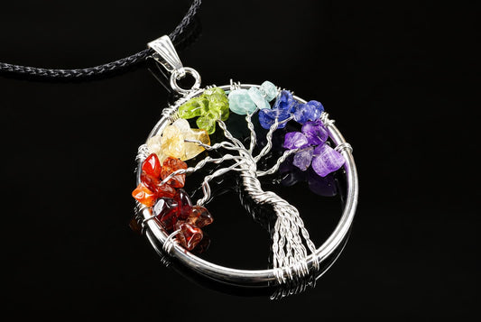 A silver-toned wire pendant shaped as a tree of life inside a circle, with multi-coloured stones along the rim on a dark surface.