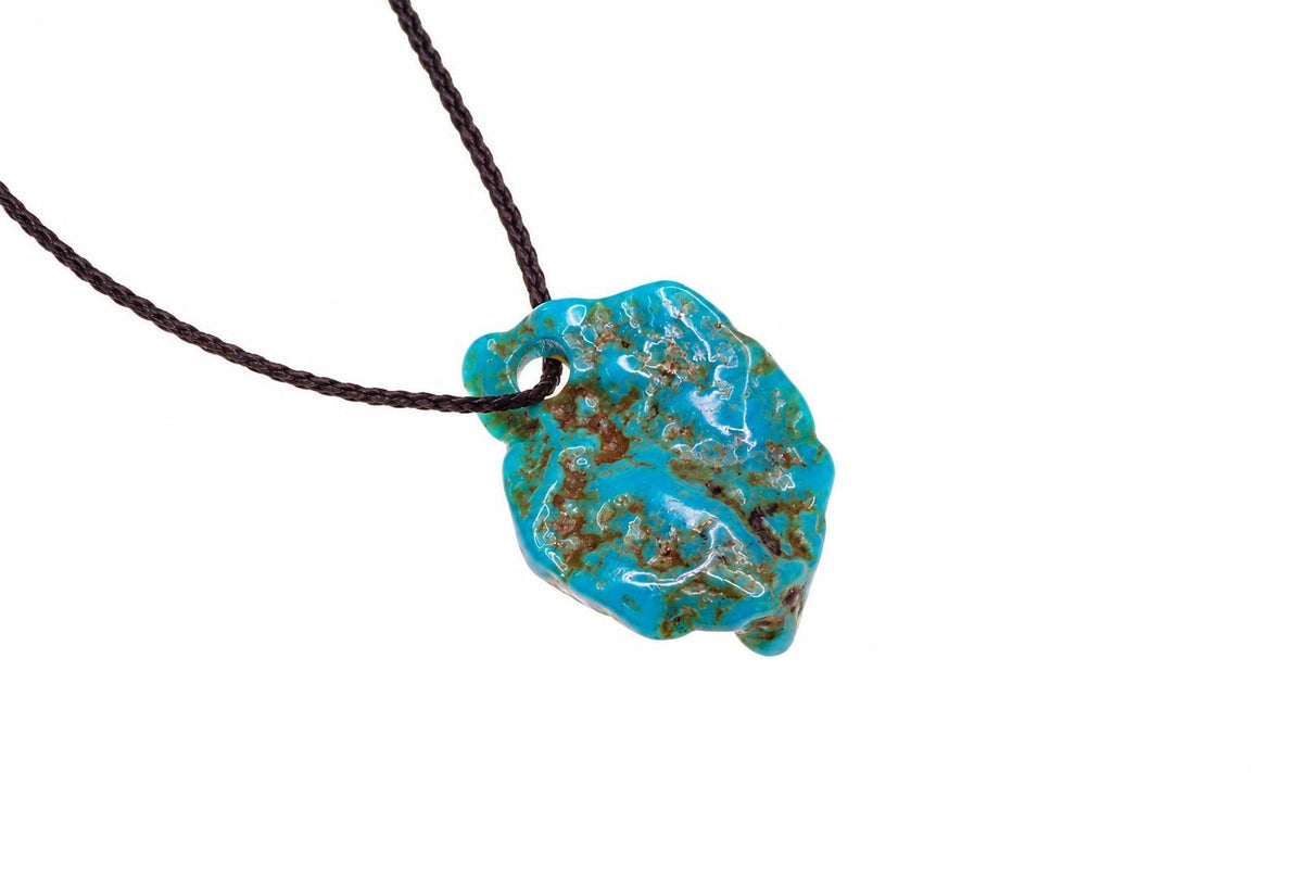 A turquoise pendant with brown matrix patterns hangs from a dark cord against a white background.
