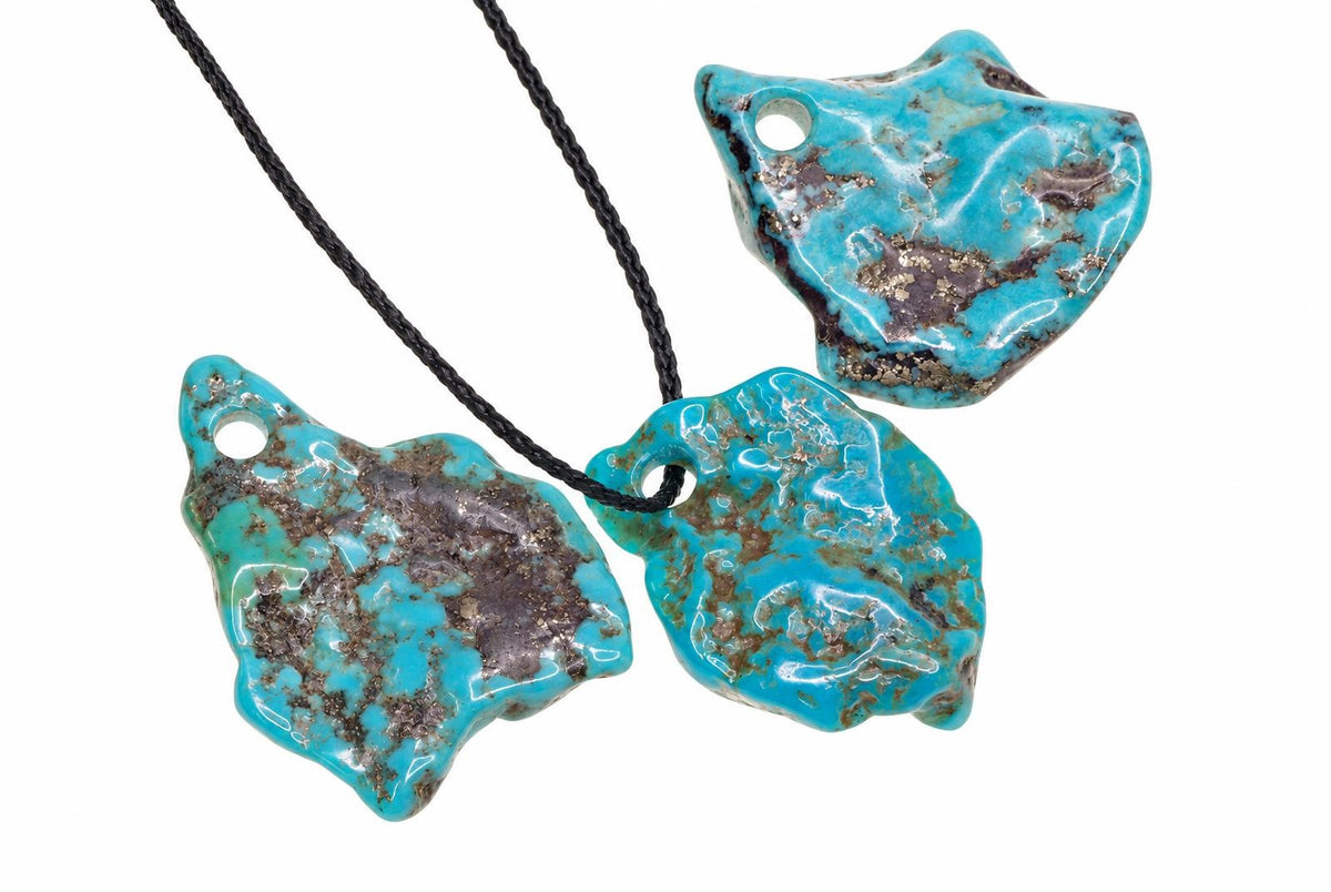 Irregular turquoise pendants have bright blue surfaces with brown veining and drilled holes, displayed with black cords against a white background.
