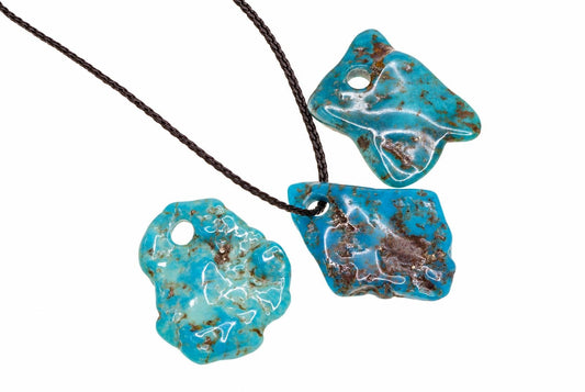 Three turquoise pendants with brown matrix on a dark cord against a white background.