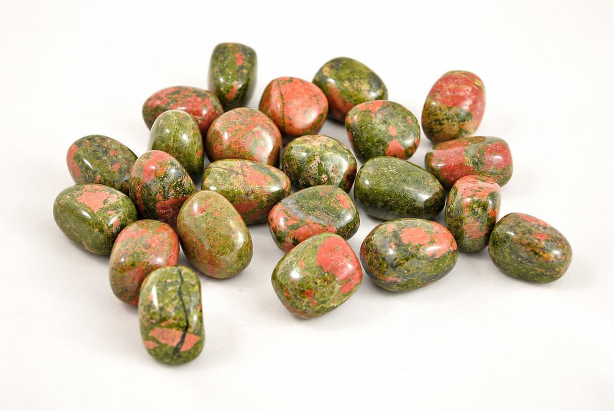 A pile of polished, oval-shaped stones with green and red patterns on a white surface.