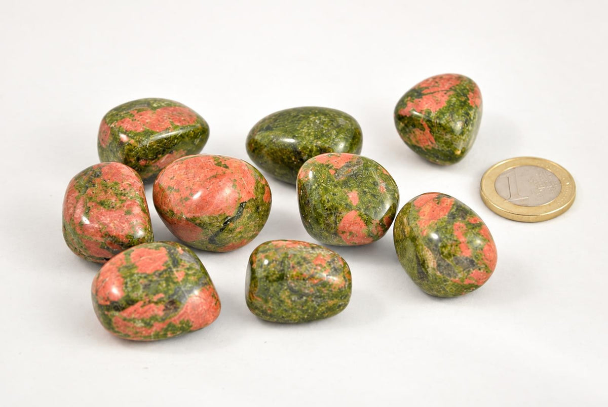 A group of polished unakite stones with green and pink patterns on a pale surface, next to a one-euro coin.