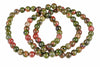 A bracelet of round beads with green, red and black speckled patterns on a white background.