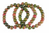 A bracelet of round beads with green and red speckled patterns, arranged in a coil on a white background.