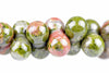 A row of round beads with pink, green and white patterns on a pale surface.