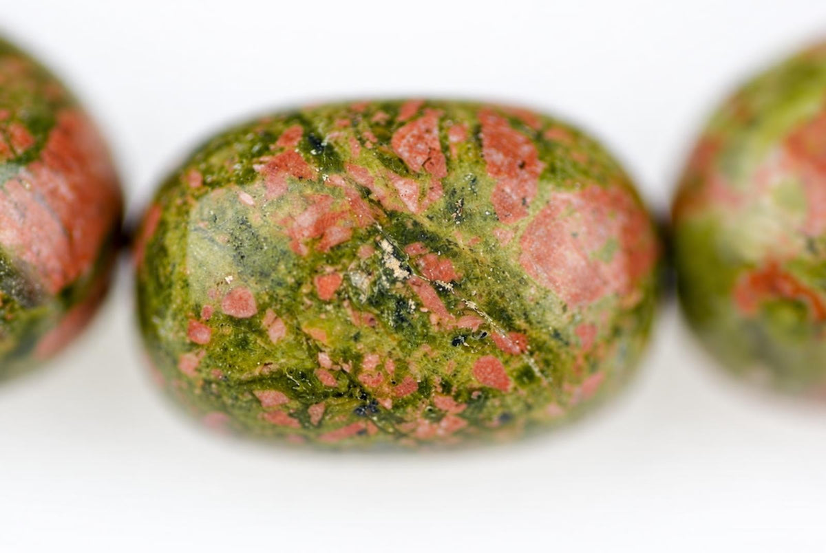 Three polished beads of green and pink speckled unakite gemstone on a pale surface.