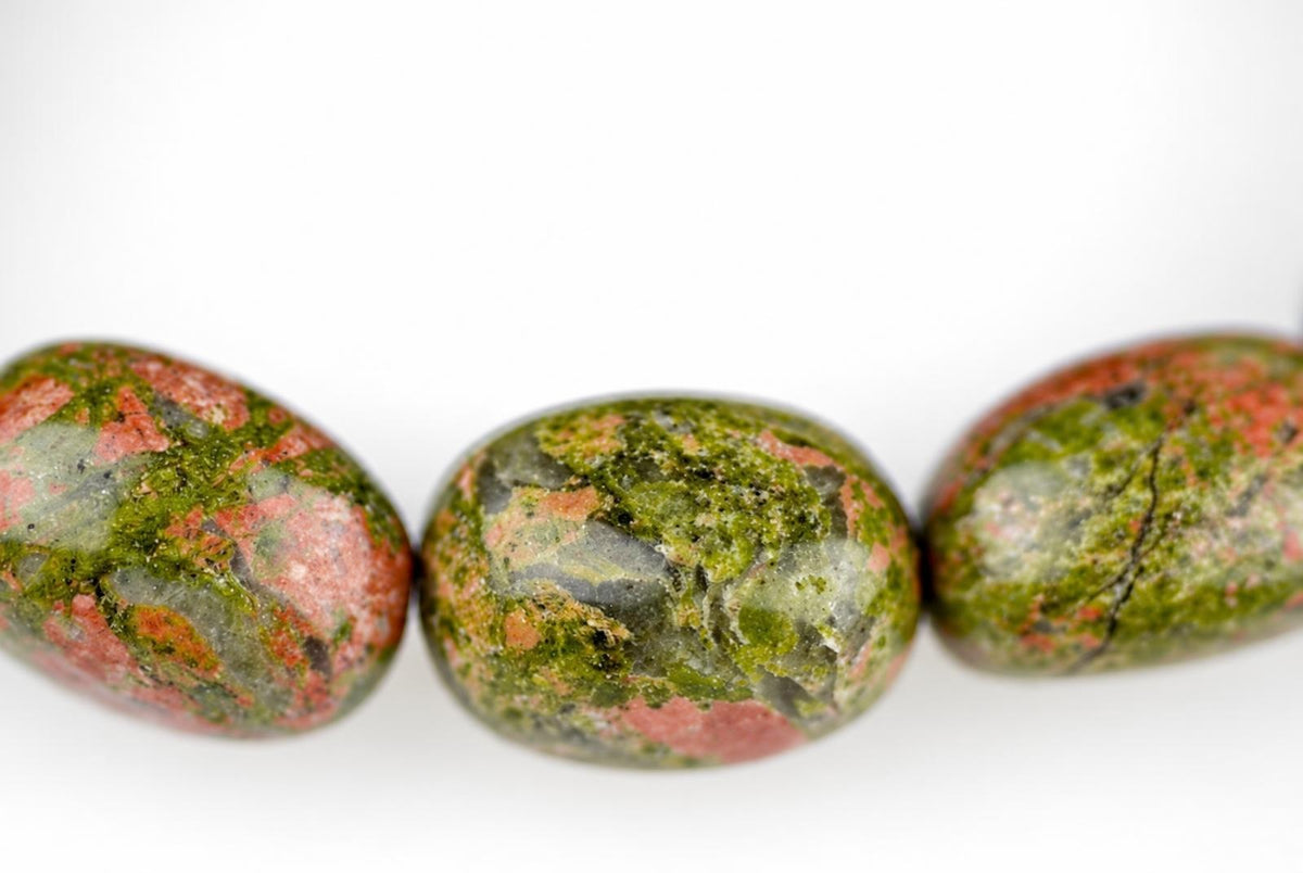 Three polished unakite beads with green, pink and grey patterns arranged in a row on a white surface.