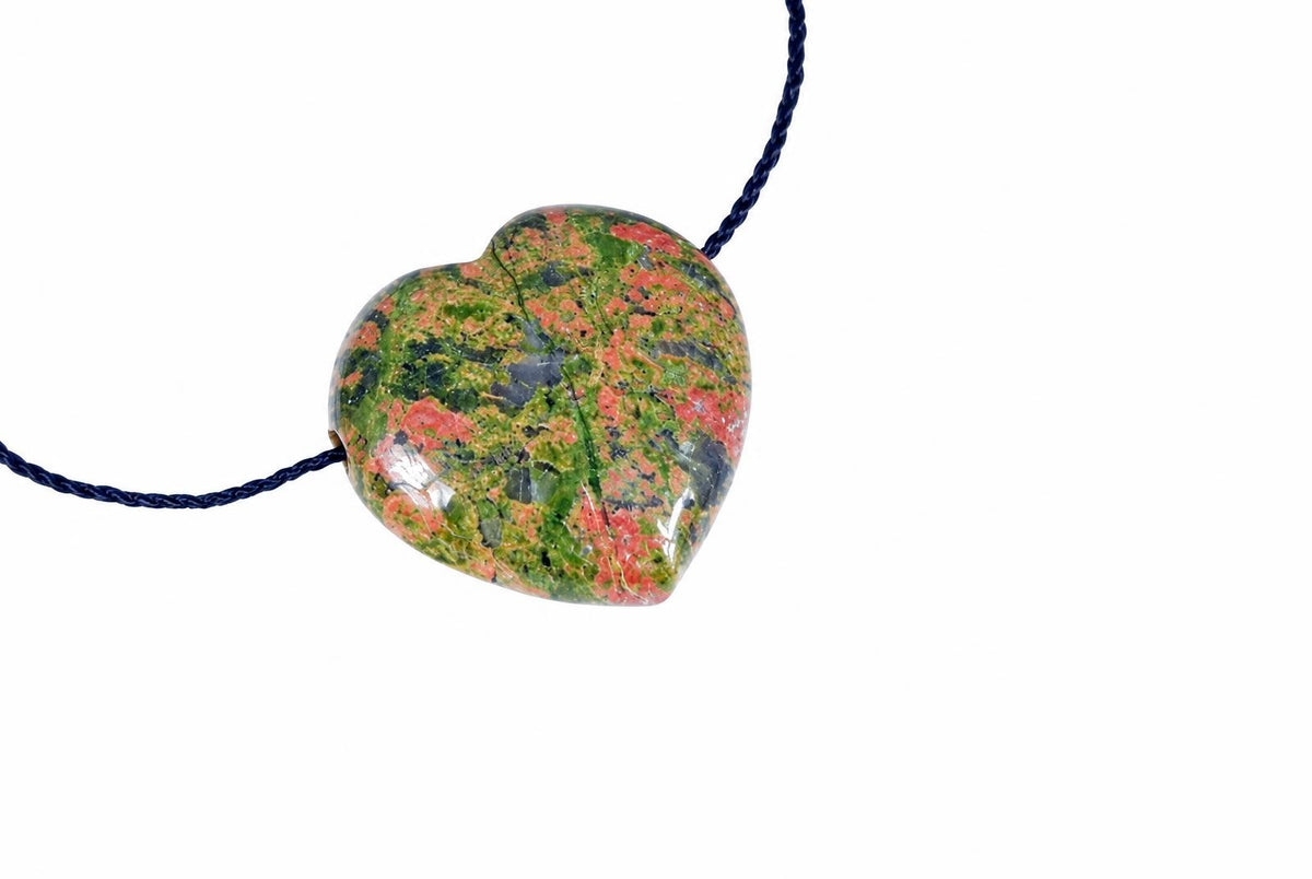A heart-shaped unakite pendant with green, red and dark patches on a dark blue cord against a white background.