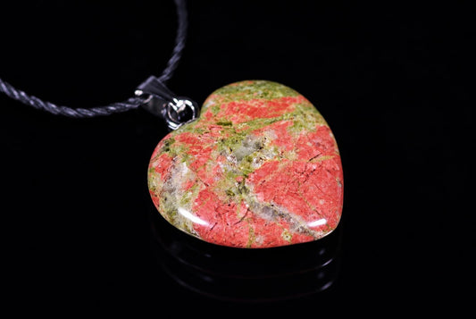 A heart-shaped pendant with red, green and white speckled stone on a dark surface.
