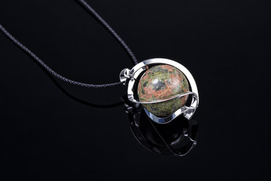 A silver-toned pendant with a round, polished unakite sphere featuring green and pink speckles on a dark surface.