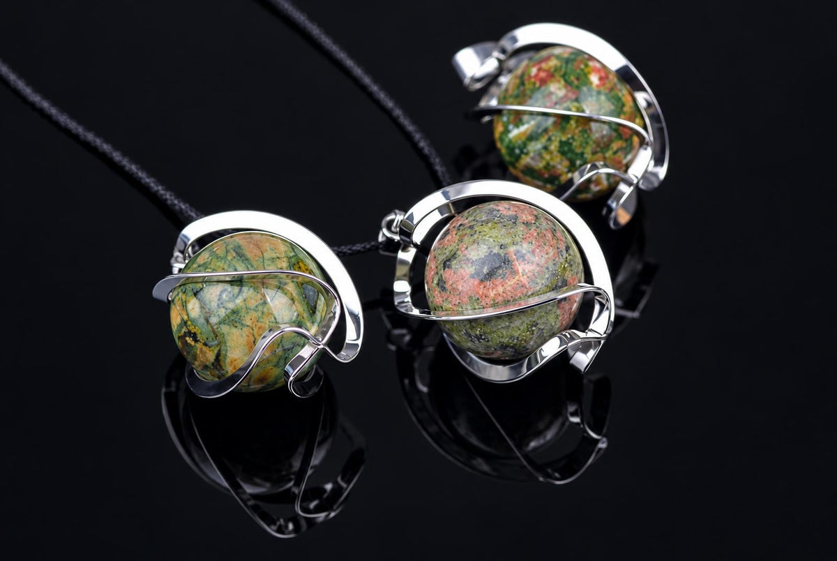 Three pendants with round, multicoloured unakite spheres in silver-toned wire settings on dark cords against a black reflective surface.