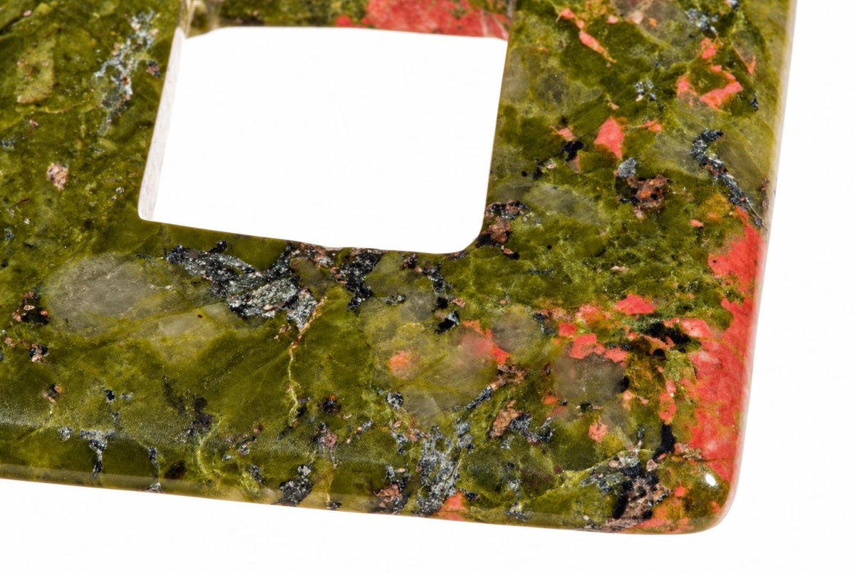 A polished square pendant with a central hole, featuring green, red, and black speckled patterns on a white background.