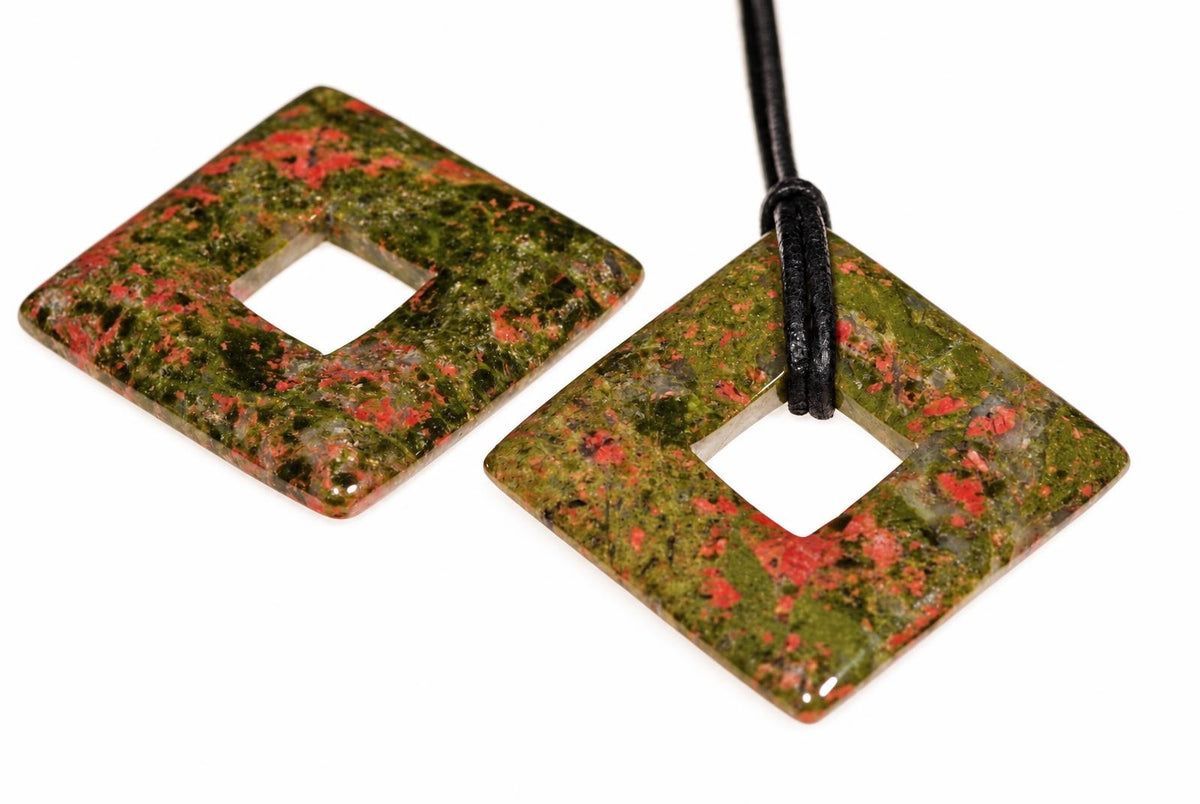 Two square, donut-shaped pendants with green and red speckled stone; one has a black cord looped through its center.