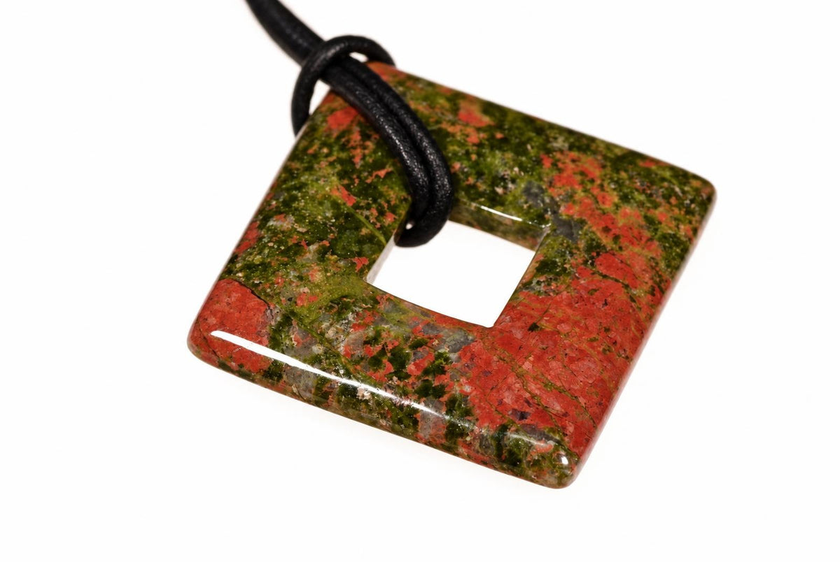 A polished square pendant with a central hole, featuring red and green speckled patterns on a dark surface.