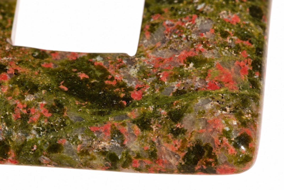 A polished square pendant with a donut hole, featuring green and red speckled unakite on a white background.