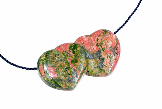 A polished, heart-shaped pendant with pink and green speckled stone on a dark blue cord against a white background.