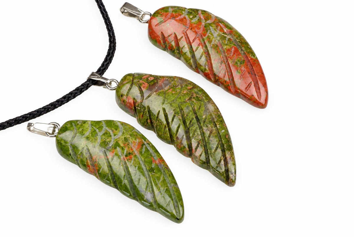 Three polished unakite pendants shaped like leaves, carved with vein details, in green and red tones on a white surface.