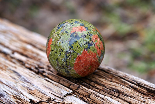 A polished sphere with green, red and dark patches rests on a weathered wooden surface.